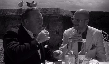 Movie still from “Cul-de-sac” (1966), directed by Roman Polanski – Two men sitting at an outdoor table drinking wine; Close Up shot, High angle