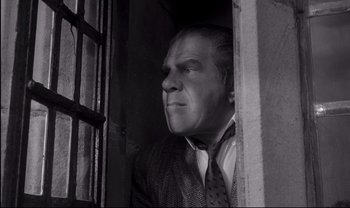 Movie still from “Cul-de-sac” (1966), directed by Roman Polanski – A man wearing a suit and tie looking out a window; Medium shot, Low angle