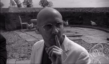Movie still from “Cul-de-sac” (1966), directed by Roman Polanski – A bald man in a white jacket and glasses; Close Up shot, Low angle