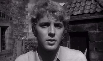 Movie still from “Cul-de-sac” (1966), directed by Roman Polanski – Black and white photograph of a young man in front of a building; Close Up shot, Low angle
