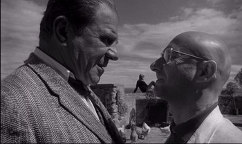 Movie still from “Cul-de-sac” (1966), directed by Roman Polanski – Two older men standing next to each other on the beach; Close Up shot, Low angle