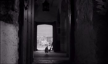 Movie still from “Cul-de-sac” (1966), directed by Roman Polanski – A black and white photo of a bird walking in an alley way; Extreme Wide shot, High angle