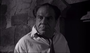 Movie still from “Cul-de-sac” (1966), directed by Roman Polanski – An older man wearing a neck tie in front of a brick wall; Close Up shot, Low angle