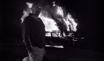 Movie still from “Cul-de-sac” (1966), directed by Roman Polanski – A man standing in front of a car on fire; Medium shot, Low angle