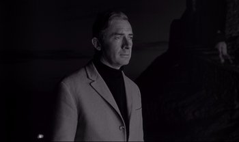 Movie still from “Cul-de-sac” (1966), directed by Roman Polanski – A man wearing a suit and a black shirt; Medium shot, Low angle