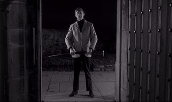 Movie still from “Cul-de-sac” (1966), directed by Roman Polanski – A black and white photo of a man holding a baseball bat; Medium shot, Low angle