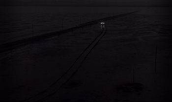 Movie still from “Cul-de-sac” (1966), directed by Roman Polanski – A car driving down a road at night; Extreme Wide shot, High angle