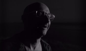 Movie still from “Cul-de-sac” (1966), directed by Roman Polanski – A man with glasses is looking at the camera; Close Up shot, Low angle