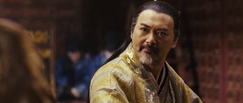 Movie still from “Curse of the Golden Flower” (2006), directed by Yimou Zhang – A man with long black hair wearing a yellow robe; Close Up shot, Over the shoulder angle
