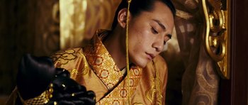 Movie still from “Curse of the Golden Flower” (2006), directed by Yimou Zhang – A man in a yellow and orange outfit with a gold chain around his neck; Close Up shot, Low angle