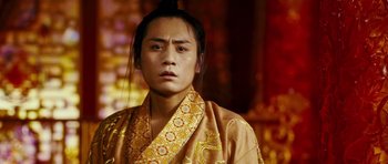 Movie still from “Curse of the Golden Flower” (2006), directed by Yimou Zhang – A man in a yellow and orange robe with long black hair; Close Up shot, Low angle