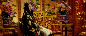 Movie still from “Curse of the Golden Flower” (2006), directed by Yimou Zhang – A woman sitting on a chair in front of flowers; Medium shot, High angle
