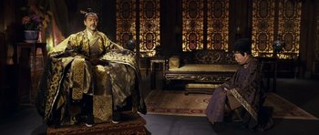 Movie still from “Curse of the Golden Flower” (2006), directed by Yimou Zhang – A man sitting in a chair next to a living room; Wide shot, High angle