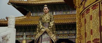 Movie still from “Curse of the Golden Flower” (2006), directed by Yimou Zhang – A man in a gold and black outfit standing in front of a building; Medium shot, Low angle