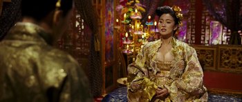 Movie still from “Curse of the Golden Flower” (2006), directed by Yimou Zhang – A woman in a gold and yellow dress in front of a chandelier; Medium shot, Over the shoulder angle