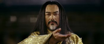 Movie still from “Curse of the Golden Flower” (2006), directed by Yimou Zhang – A man with long black hair wearing a gold robe; Close Up shot, Low angle
