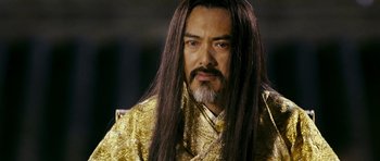 Movie still from “Curse of the Golden Flower” (2006), directed by Yimou Zhang – A man with long black hair wearing a gold robe; Close Up shot, Over the shoulder angle