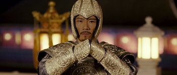 Movie still from “Curse of the Golden Flower” (2006), directed by Yimou Zhang – A man in a suit of a knight with his hands clasped together; Close Up shot, Low angle