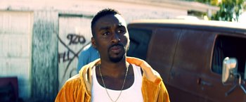 Movie still from “Cut Throat City” (2020), directed by RZA – A man in a white tank top and a yellow jacket; Close Up shot, Over the shoulder angle