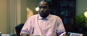 Movie still from “Cut Throat City” (2020), directed by RZA – A man sitting at a table looking at the camera; Close Up shot, Low angle