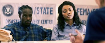 Movie still from “Cut Throat City” (2020), directed by RZA – A man and a woman sitting in front of each other in front of a sign; Medium shot, Over the shoulder angle