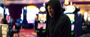 Movie still from “Cut Throat City” (2020), directed by RZA – A man in a black hooded jacket in front of a slot machine; Close Up shot, Low angle