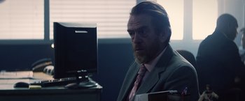 Movie still from “Cut Throat City” (2020), directed by RZA – A man in a suit sitting in front of a computer monitor; Close Up shot, Over the shoulder angle