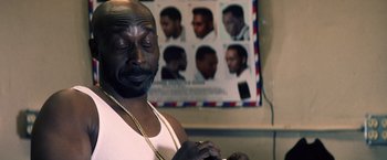 Movie still from “Cut Throat City” (2020), directed by RZA – A black man with a beard and a white tank top; Close Up shot, Over the shoulder angle