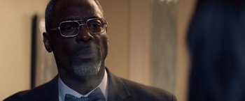 Movie still from “Cut Throat City” (2020), directed by RZA – A person wearing a suit and glasses; Close Up shot, Over the shoulder angle
