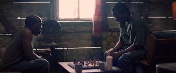 Movie still from “Cut Throat City” (2020), directed by RZA – A man sitting at a table playing a game of chess; Medium shot, Over the shoulder angle