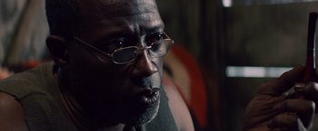 Movie still from “Cut Throat City” (2020), directed by RZA – An older man wearing glasses looking at the camera; Close Up shot, Low angle