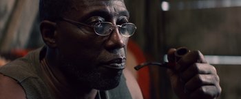 Movie still from “Cut Throat City” (2020), directed by RZA – An older man wearing glasses and holding a pipe in his mouth; Close Up shot, Low angle