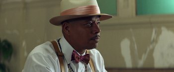 Movie still from “Cut Throat City” (2020), directed by RZA – A person wearing a hat and a bow tie; Close Up shot, Over the shoulder angle