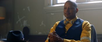 Movie still from “Cut Throat City” (2020), directed by RZA – A man sitting in front of a window holding a cell phone; Close Up shot, Over the shoulder angle