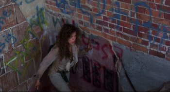 Movie still from “Cyborg” (1989), directed by Albert Pyun – A woman in a white shirt is climbing up a wall; Medium shot, Low angle