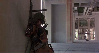 Movie still from “Cyborg” (1989), directed by Albert Pyun – A woman dressed as a character from star wars is leaning against a wall; Wide shot, Low angle