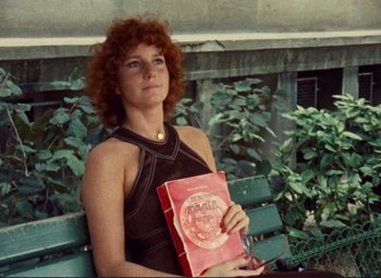 Movie still from “Celine and Julie Go Boating” (1974), directed by Jacques Rivette – A woman sitting on top of a wooden bench holding a book; Medium shot, High angle