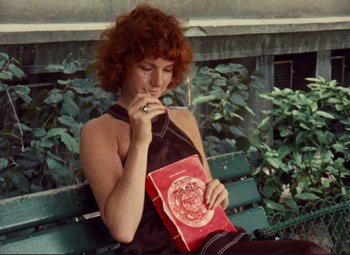 Movie still from “Celine and Julie Go Boating” (1974), directed by Jacques Rivette – A woman sitting on top of a wooden bench holding a book; Medium shot, High angle