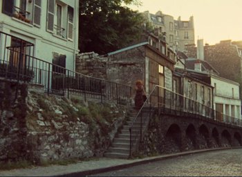 Movie still from “Celine and Julie Go Boating” (1974), directed by Jacques Rivette – A woman walking down a set of stairs on the side of a road; Extreme Wide shot, High angle