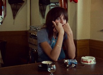 Movie still from “Celine and Julie Go Boating” (1974), directed by Jacques Rivette – A woman sitting at a table with her hand on her face; Medium shot, High angle