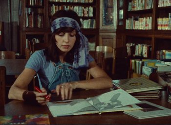 Movie still from “Celine and Julie Go Boating” (1974), directed by Jacques Rivette – A woman sitting at a table in front of an open book; Medium shot, High angle