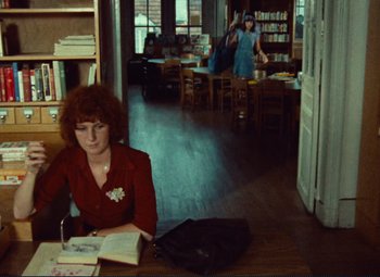 Movie still from “Celine and Julie Go Boating” (1974), directed by Jacques Rivette – A woman sitting at a table with a book in her lap; Wide shot, High angle