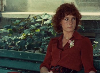 Movie still from “Celine and Julie Go Boating” (1974), directed by Jacques Rivette – A woman sitting on top of a wooden bench next to plants; Medium shot, High angle