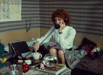 Movie still from “Celine and Julie Go Boating” (1974), directed by Jacques Rivette – A woman sitting at a table talking on the phone; Medium shot, High angle
