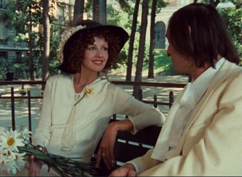 Movie still from “Celine and Julie Go Boating” (1974), directed by Jacques Rivette – A woman wearing a hat sitting next to a man on a park bench; Medium shot, Over the shoulder angle