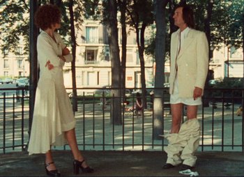 Movie still from “Celine and Julie Go Boating” (1974), directed by Jacques Rivette – A man and a woman standing next to each other on a sidewalk; Wide shot, Low angle