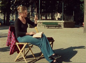 Movie still from “Celine and Julie Go Boating” (1974), directed by Jacques Rivette – A woman sitting in a chair with a book in her hand; Wide shot, High angle