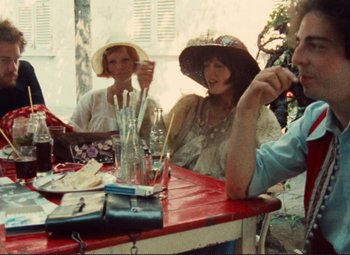 Movie still from “Celine and Julie Go Boating” (1974), directed by Jacques Rivette – A group of people sitting at a table with drinks; Medium shot, Over the shoulder angle