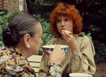 Movie still from “Celine and Julie Go Boating” (1974), directed by Jacques Rivette – Two women sitting at an outdoor table eating food; Medium shot, Over the shoulder angle