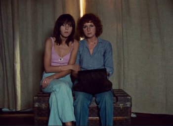 Movie still from “Celine and Julie Go Boating” (1974), directed by Jacques Rivette – Two women sitting next to each other in front of a curtain; Medium shot, High angle